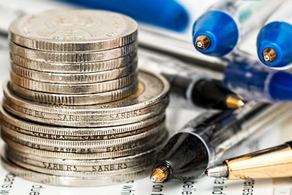 Das Bild zeigt eine Finanzkalkulation, auf welcher diverse Münzen und Stifte liegen, in Nahaufnahme.