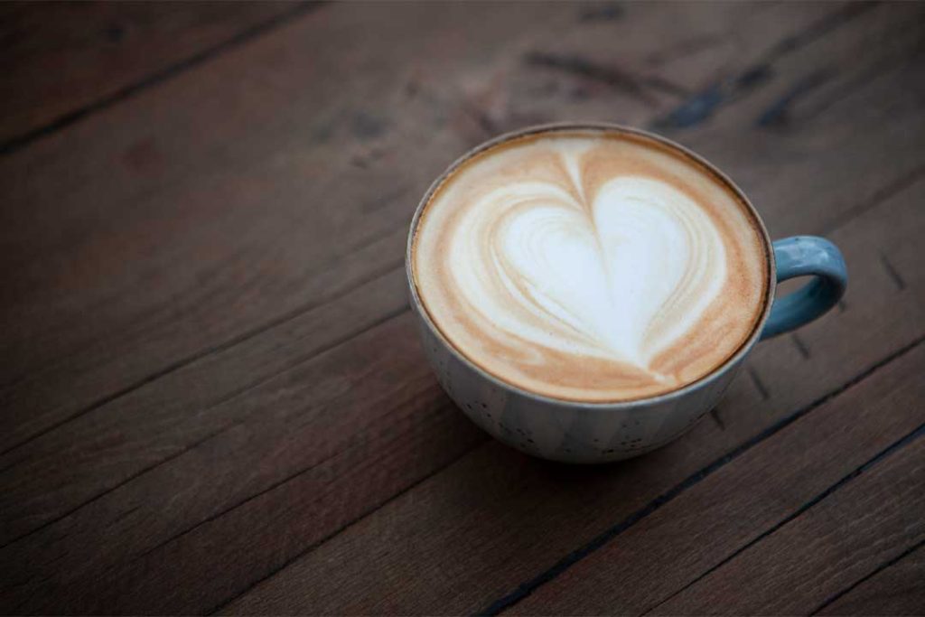 Das Bild zeigt eine Tasse Cappuccino, welche auf einem Tisch steht.