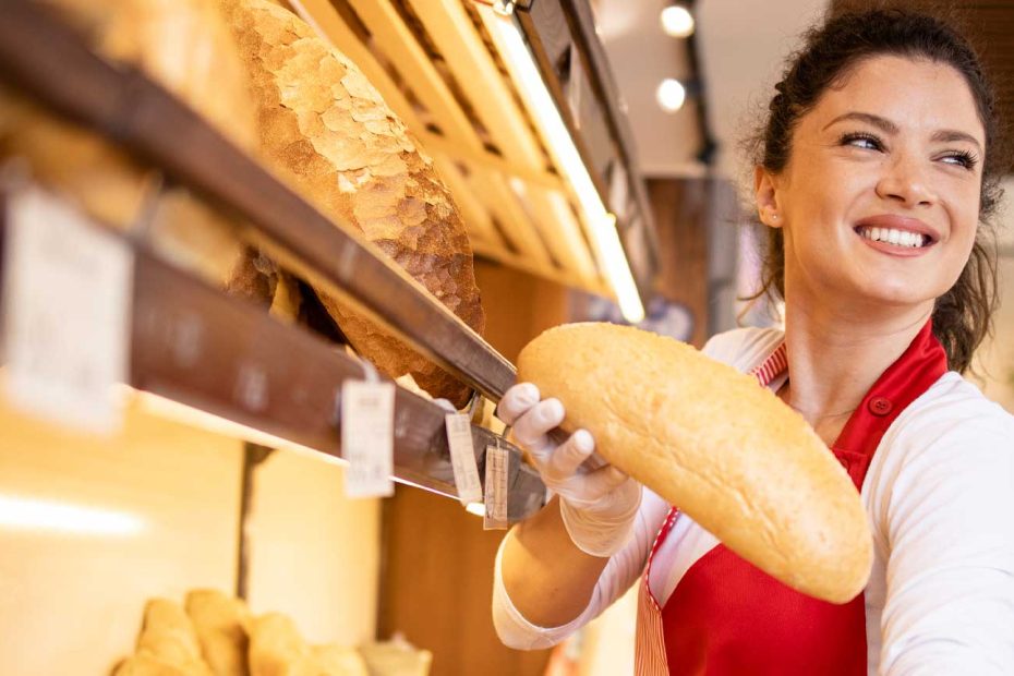 Das Bild zeigt eine Bäckereifachverkäuferin, welche ein Brötchen in der Hand hält.